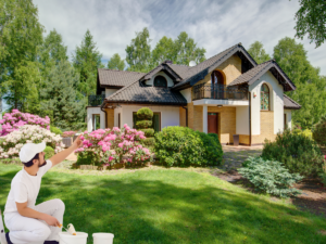 Why Now Is the Perfect Time to Paint - Painter pointing to the house with a roller in his hand.