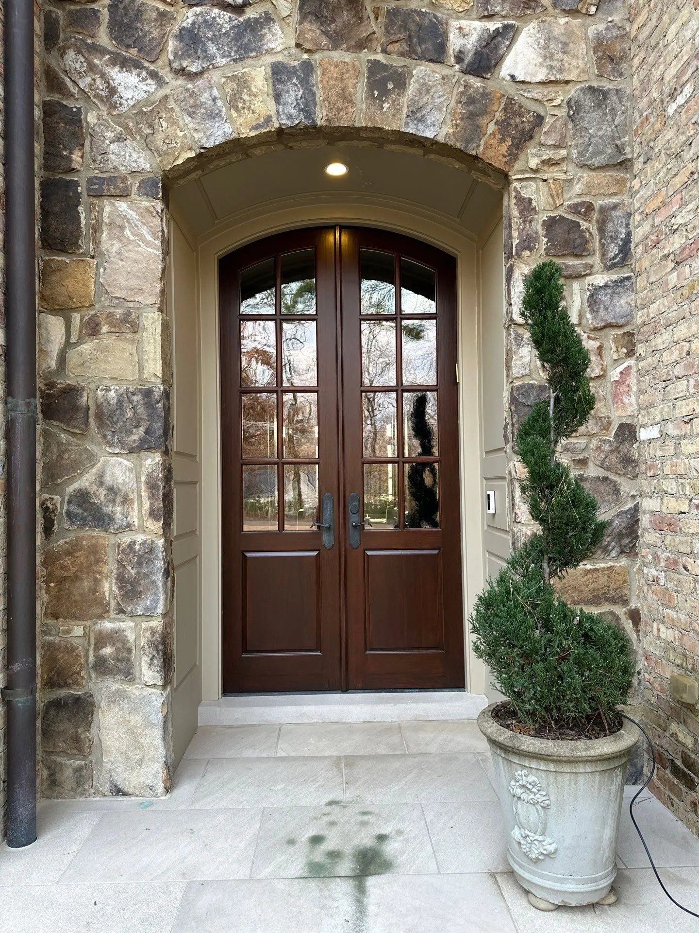 Door Painting and Wood Staining North Atlanta Elegant dark wood double entry doors with glass panels in a stone archway in North Atlanta.