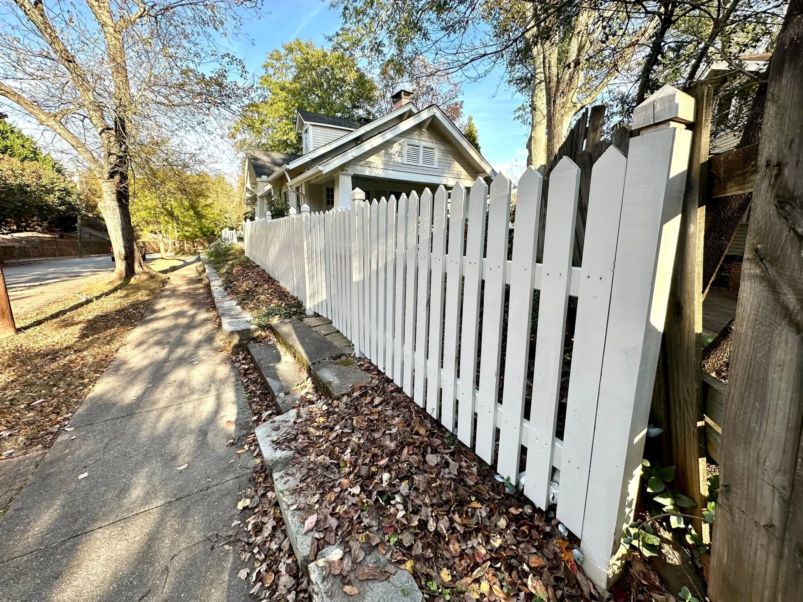 Fence Painting and Staining North Atlanta Newly painted white picket fence along a sidewalk in front of a house in North Atlanta.