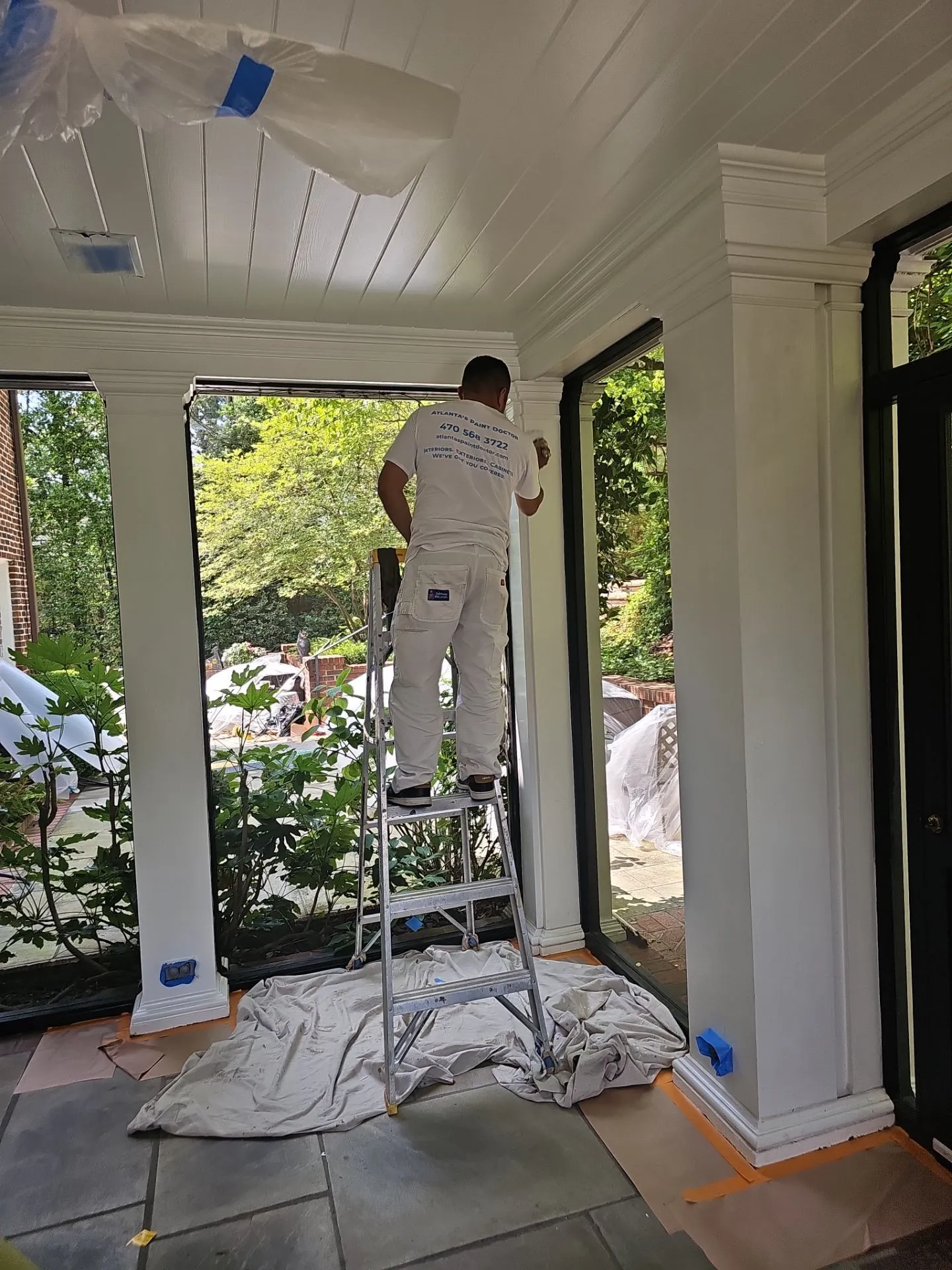 Interior Trim Painting North Atlanta Painter on a ladder carefully painting white interior trim in a sunroom, providing trim painting in North Atlanta.