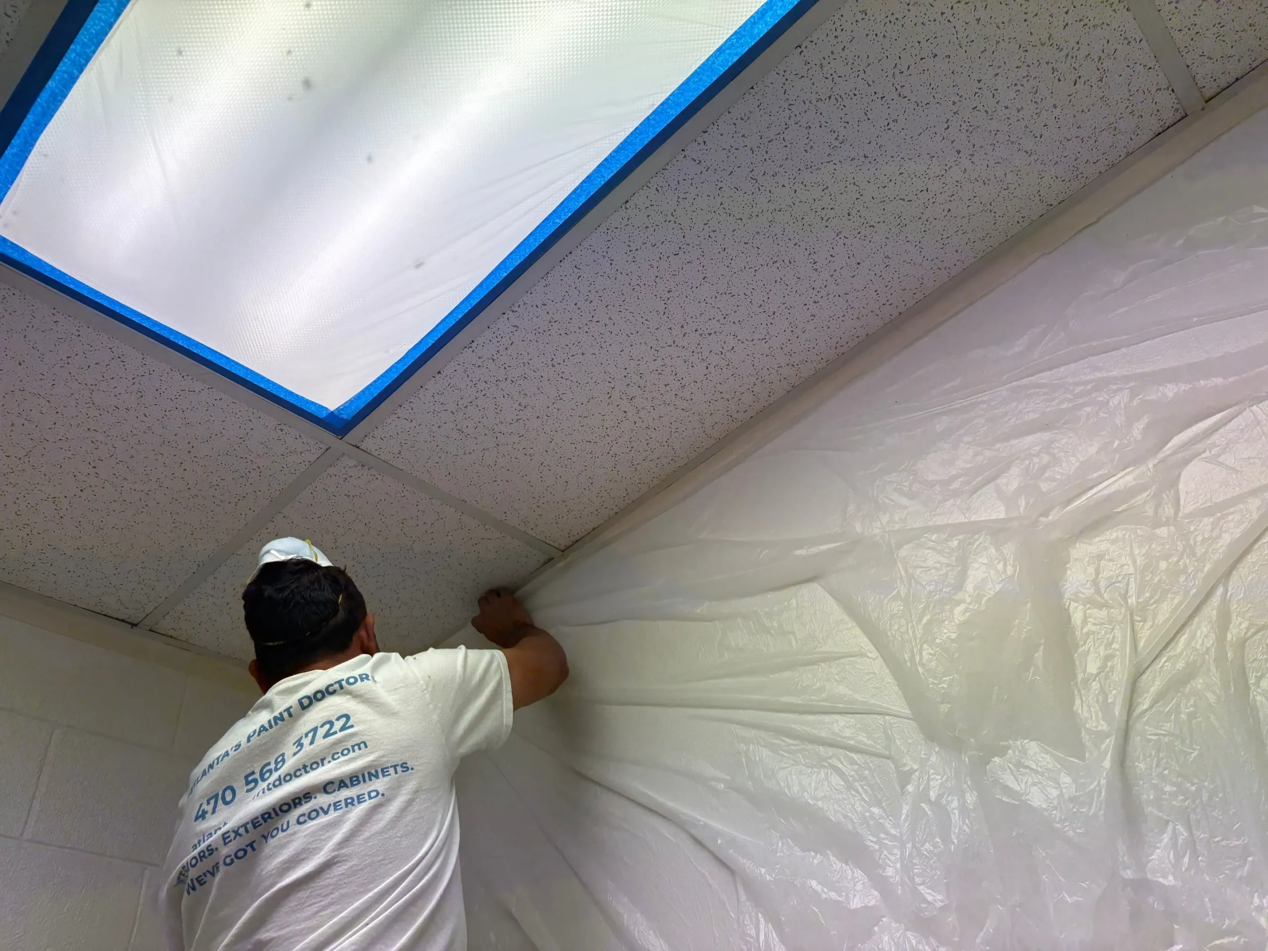 Commercial Interior Painting Preparation North Atlanta Painter taping plastic sheeting for protection during commercial interior painting in North Atlanta.