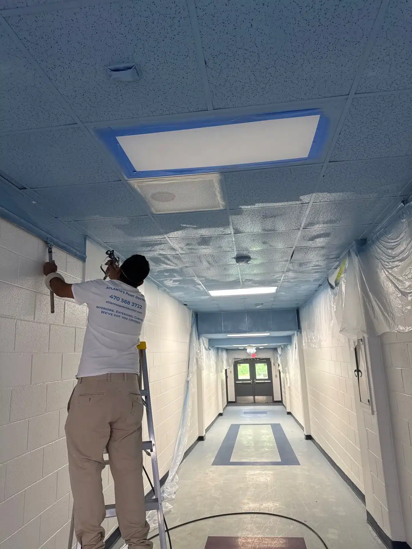 Commercial Ceiling Painting in North Atlanta Painter using a spray gun to paint a blue ceiling in a commercial hallway in North Atlanta.