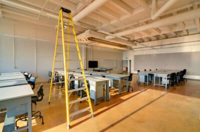 Commercial Office Interior Painting Cream-painted commercial interior with yellow ladder, wooden flooring, and industrial ceiling infrastructure.