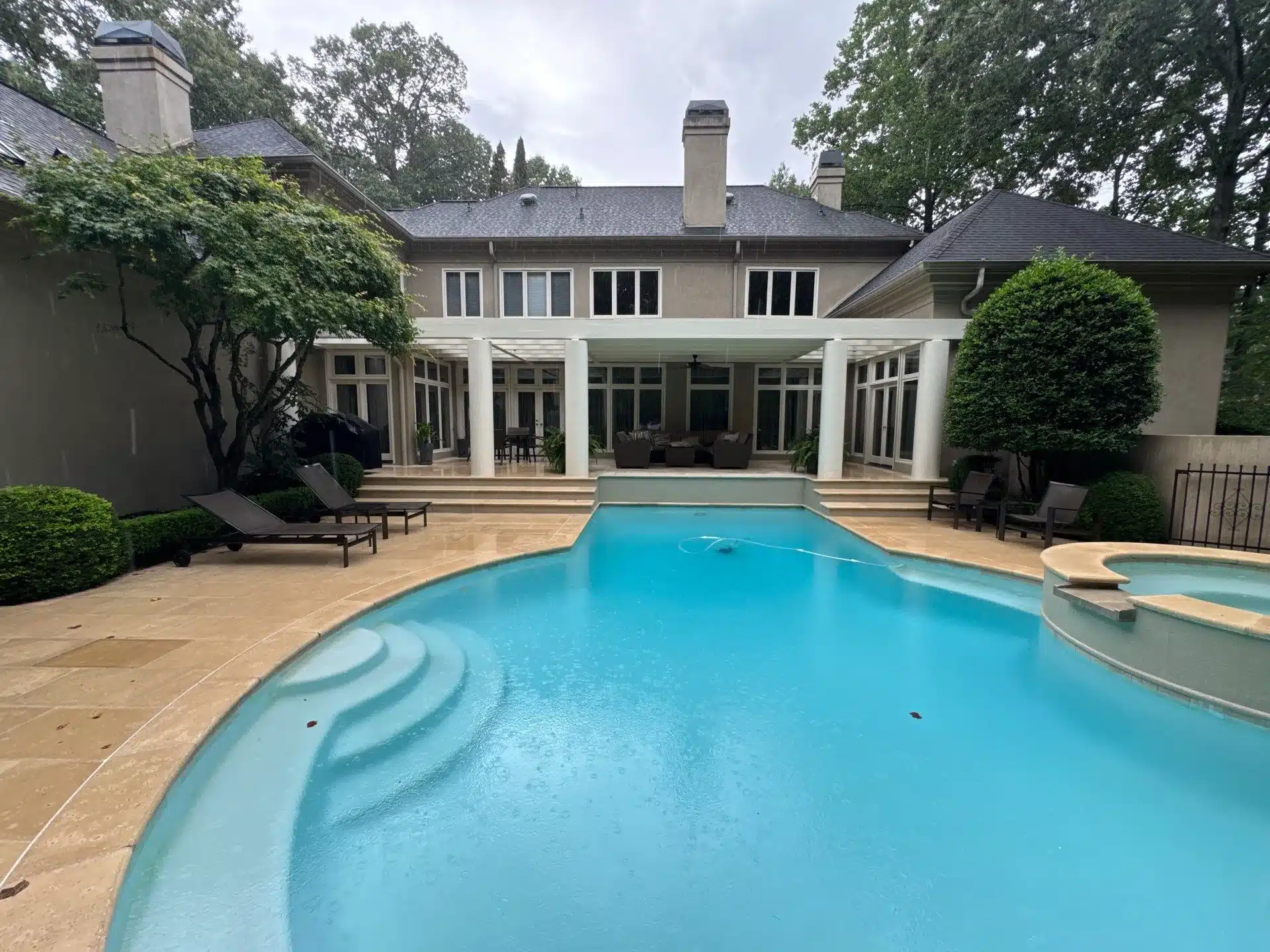 Beige Residential Home With White Columns Beige and cream painted residential home exterior with white columns, dark roof, and multi-pane windows overlooking pool