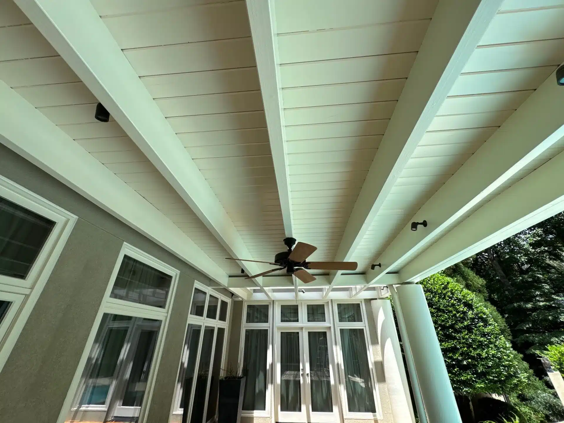 Cream Painted Pergola Ceiling Cream-painted wooden pergola with white beams, horizontal slat ceiling, ceiling fan, and multi-pane glass doors.